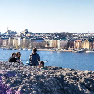 A group of people sit at a high point above a waterside city enjoying the view in the late evening sunshine; Stockholm, Sweden.