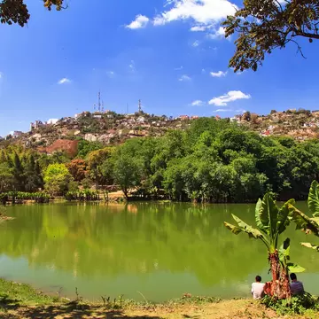 Calm green lake edged with trees below a hillside of houses in Antananarivo, Madagascar.