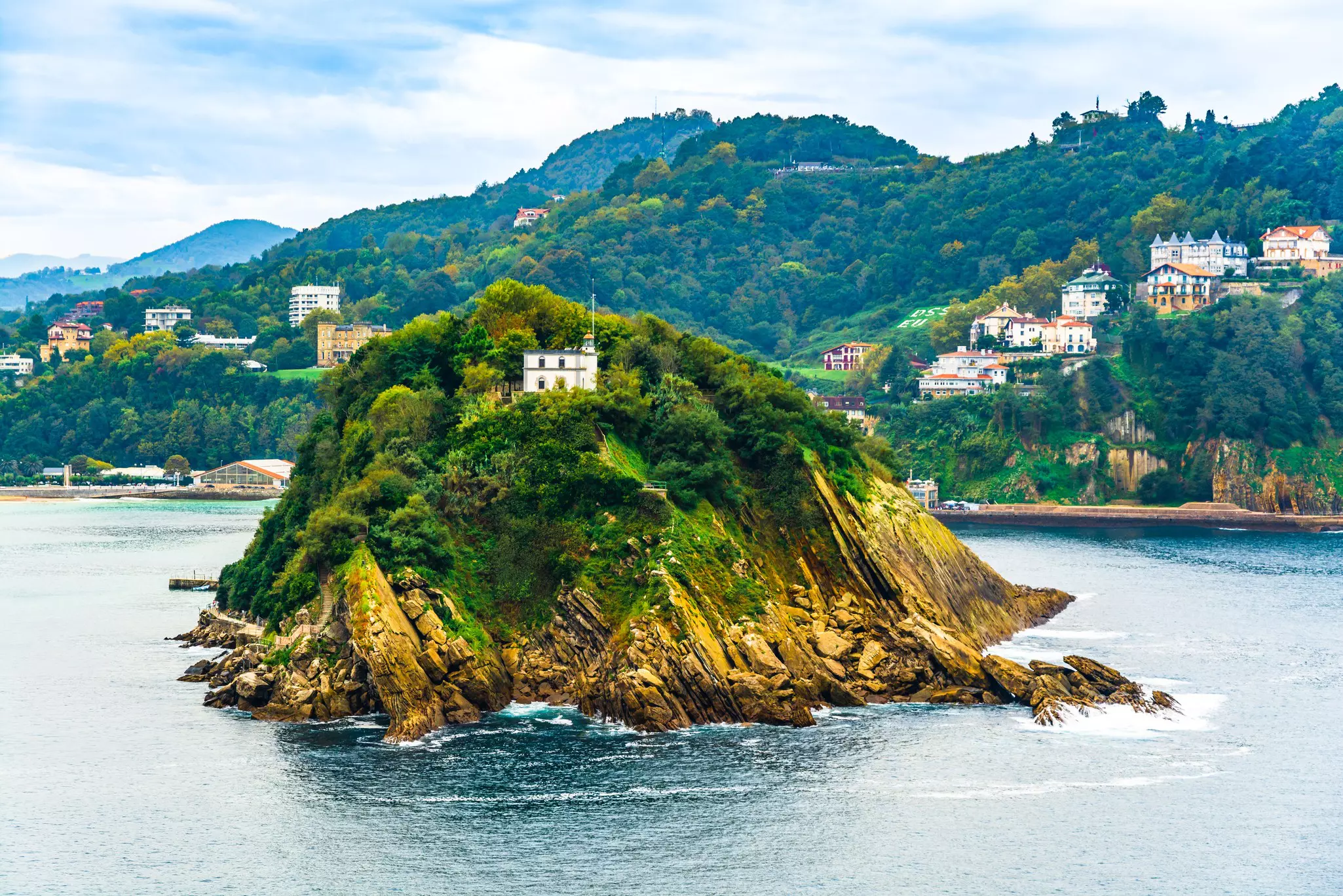 A rocky islet with one central building at its peak, just off the shore of the mainland.