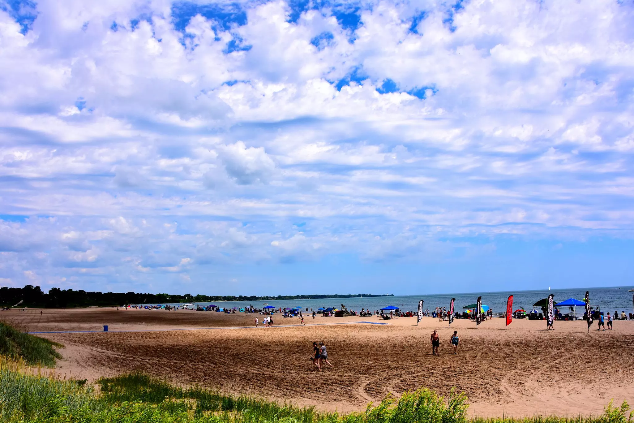 Many people enjoying the beach activities at North Beach on a beautiful summer day with clouded skies above the cool waters of Lake Michigan