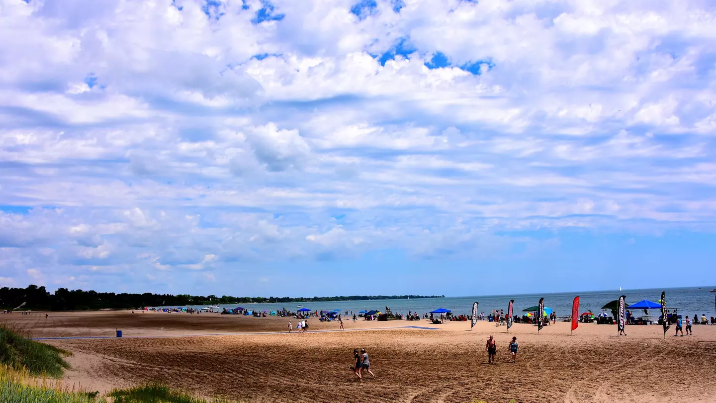 Many people enjoying the beach activities at North Beach on a beautiful summer day with clouded skies above the cool waters of Lake Michigan