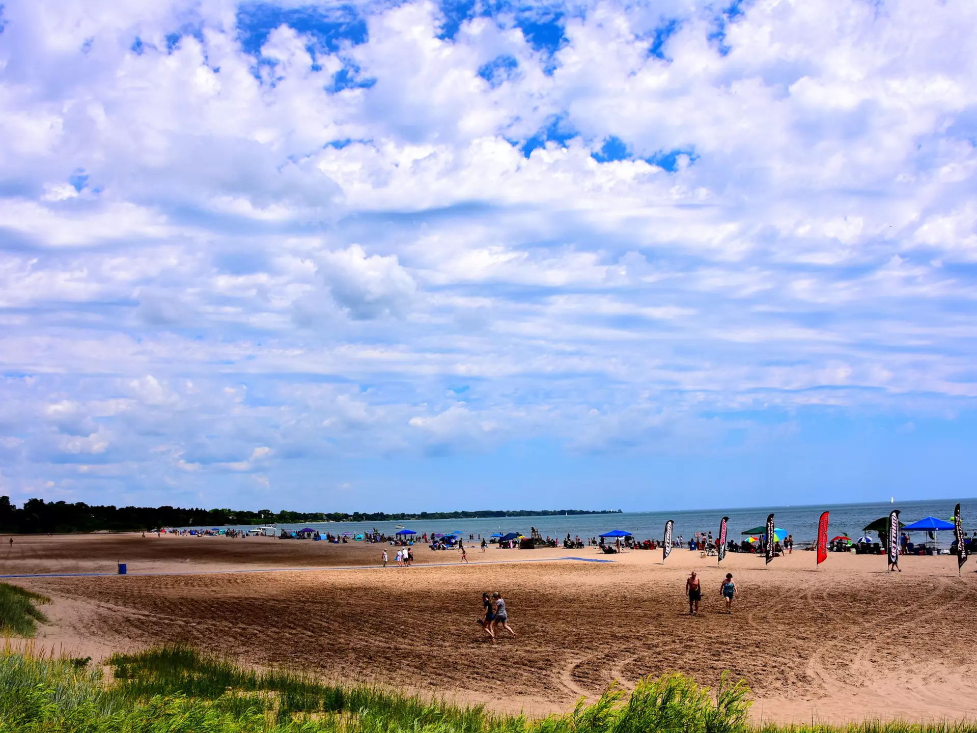 Many people enjoying the beach activities at North Beach on a beautiful summer day with clouded skies above the cool waters of Lake Michigan