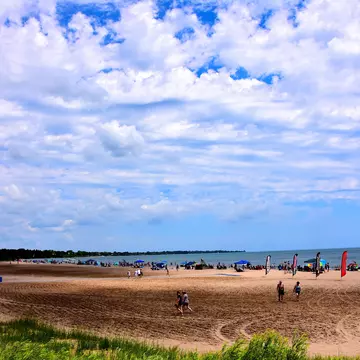 Many people enjoying the beach activities at North Beach on a beautiful summer day with clouded skies above the cool waters of Lake Michigan