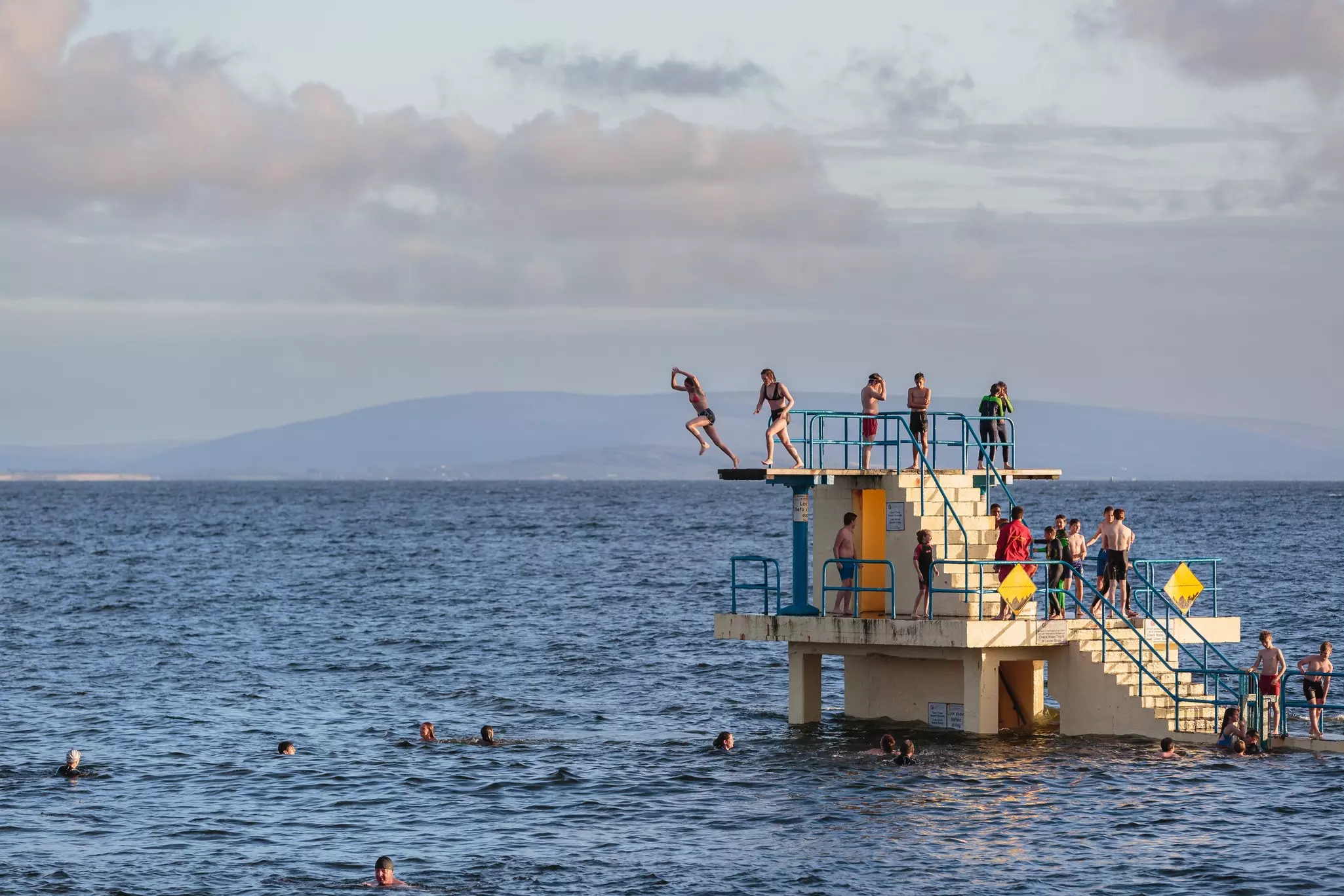 People jump from a diving tower in Galway at high tide.