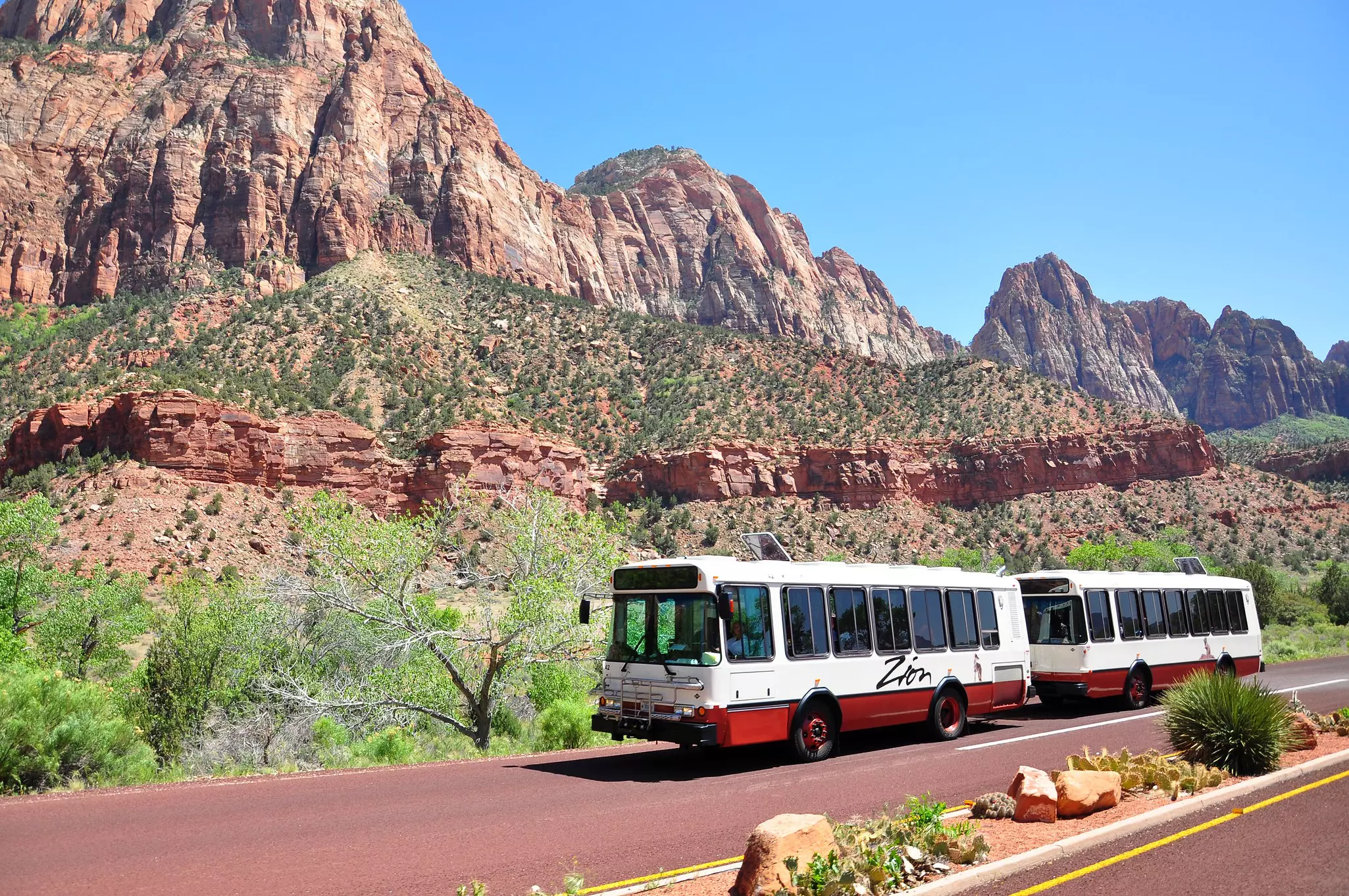 A bus with two separate compartments drive on a road through a red-rock canyon