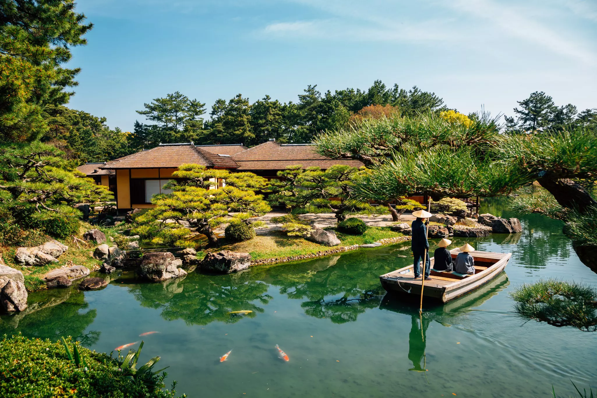 A small wooden boat travels through an ornamental lake in a beautiful Japanese garden. 