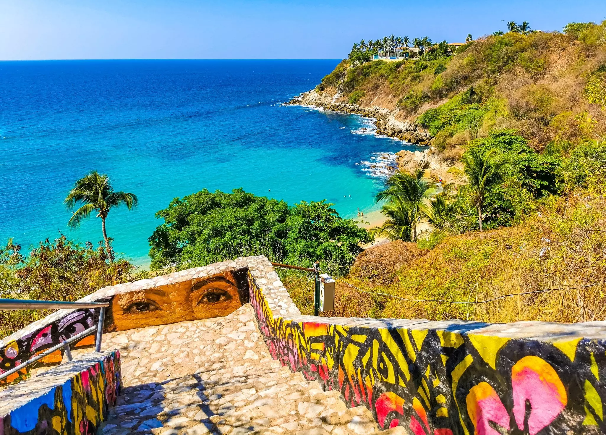 Stone stairs with paintings; turquoise blue water and palm trees are below.