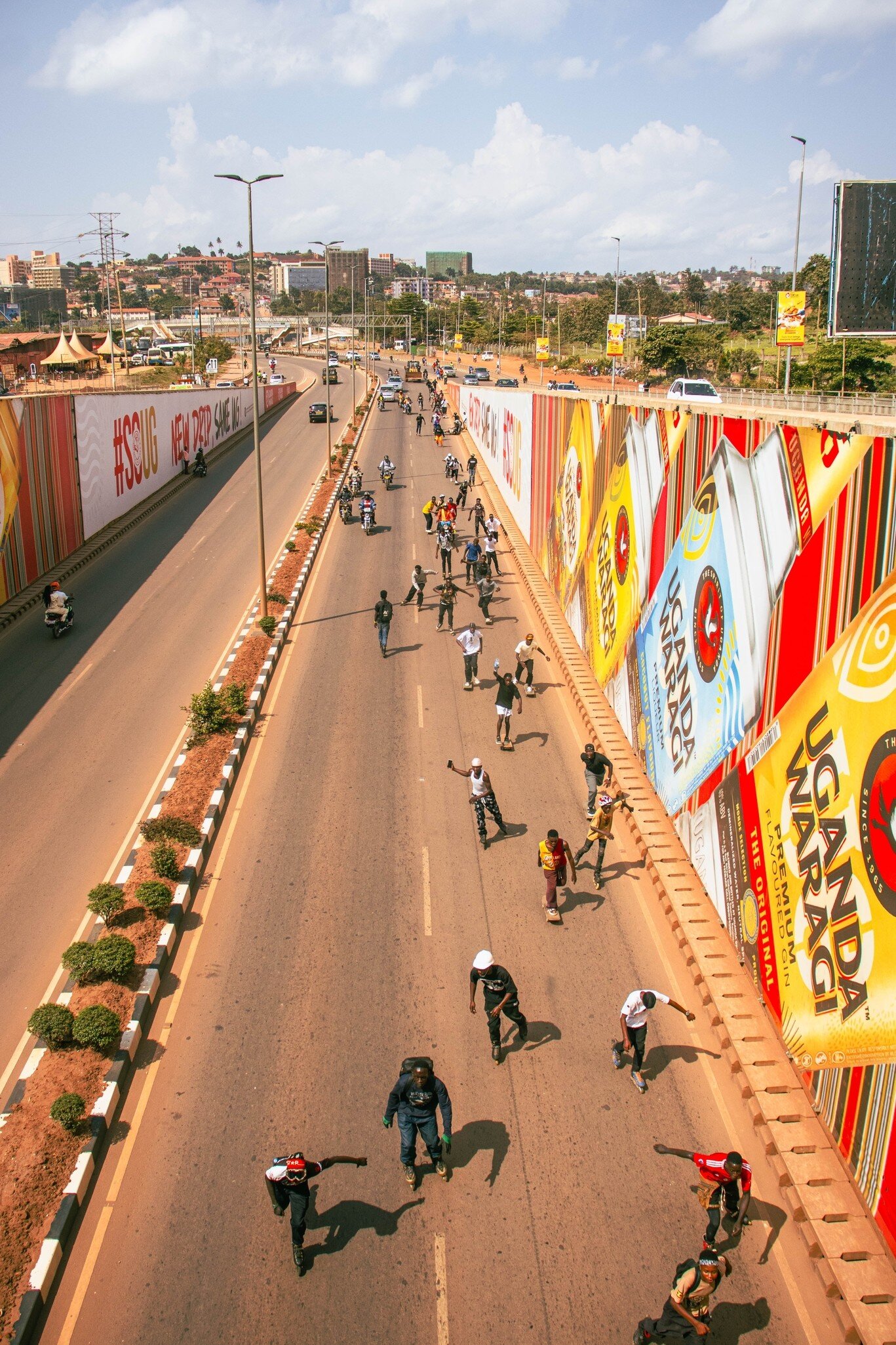 Skaters roll down a Kampala road past billboards in Uganda; ads read UGANDA WARAGI and #SOUG NEW DRIP SAME UG