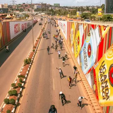 Skaters roll down a Kampala road past billboards in Uganda; ads read UGANDA WARAGI and #SOUG NEW DRIP SAME UG