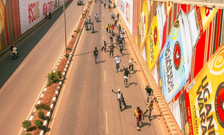 Skaters roll down a Kampala road past billboards in Uganda; ads read UGANDA WARAGI and #SOUG NEW DRIP SAME UG