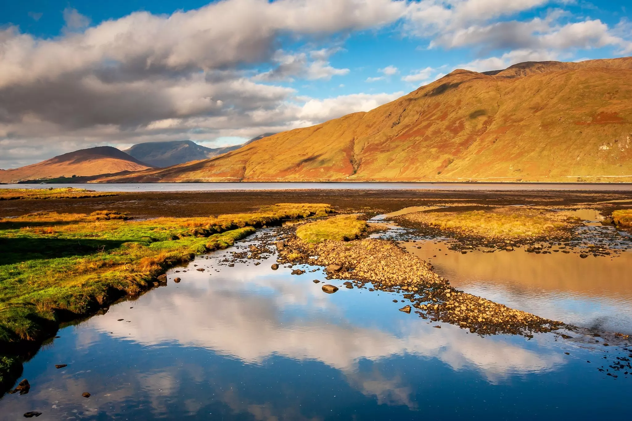 The head of a glacial fjord with glassy water and golden hills in the distance, Connemara