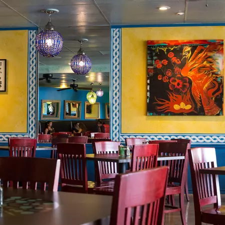 yellow walls with bright artwork behind tables with red chairs at a restaurant 