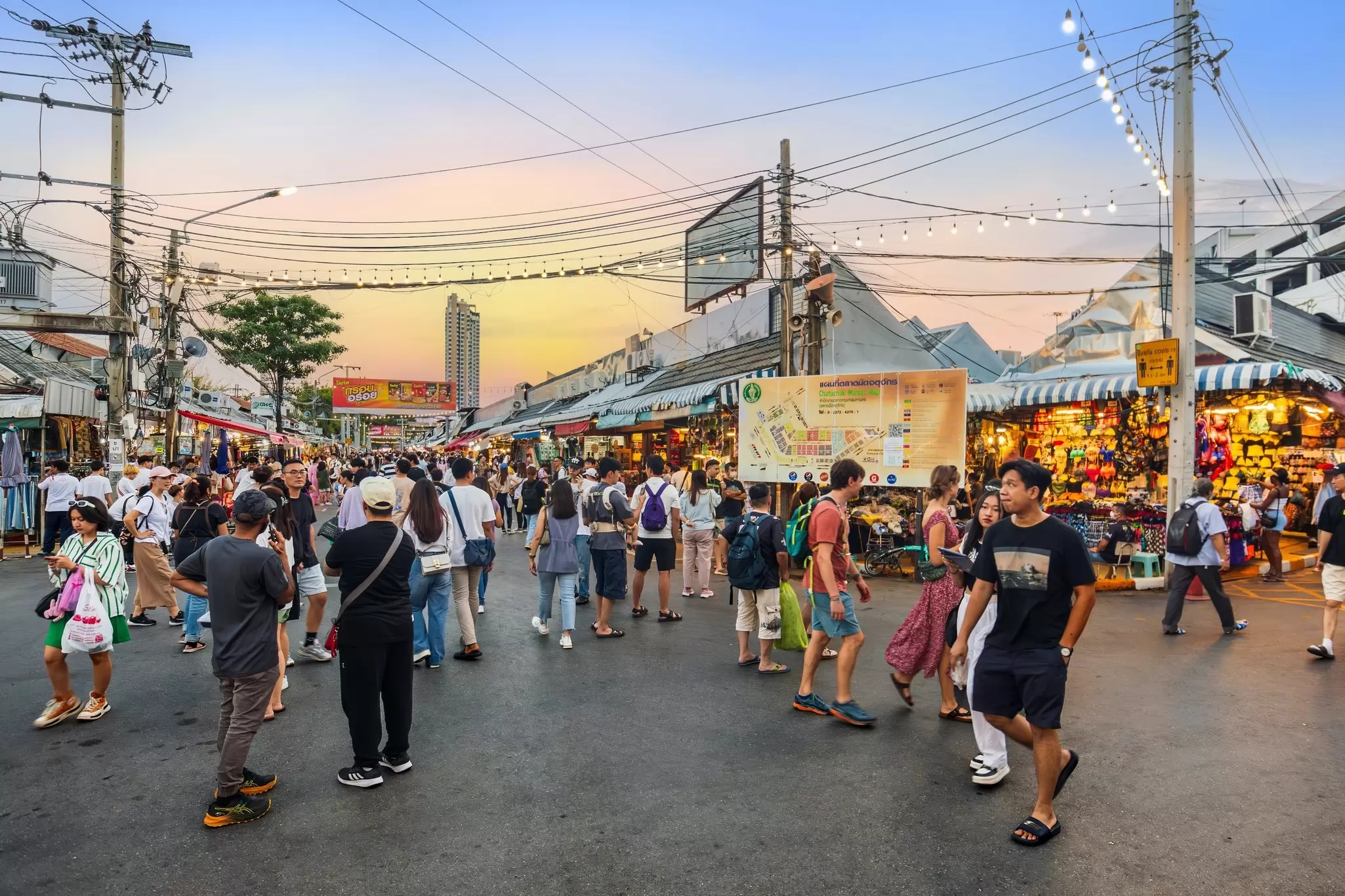 People exploring Chatuchak Weekend Market at sunset in Bangkok, Thailand.