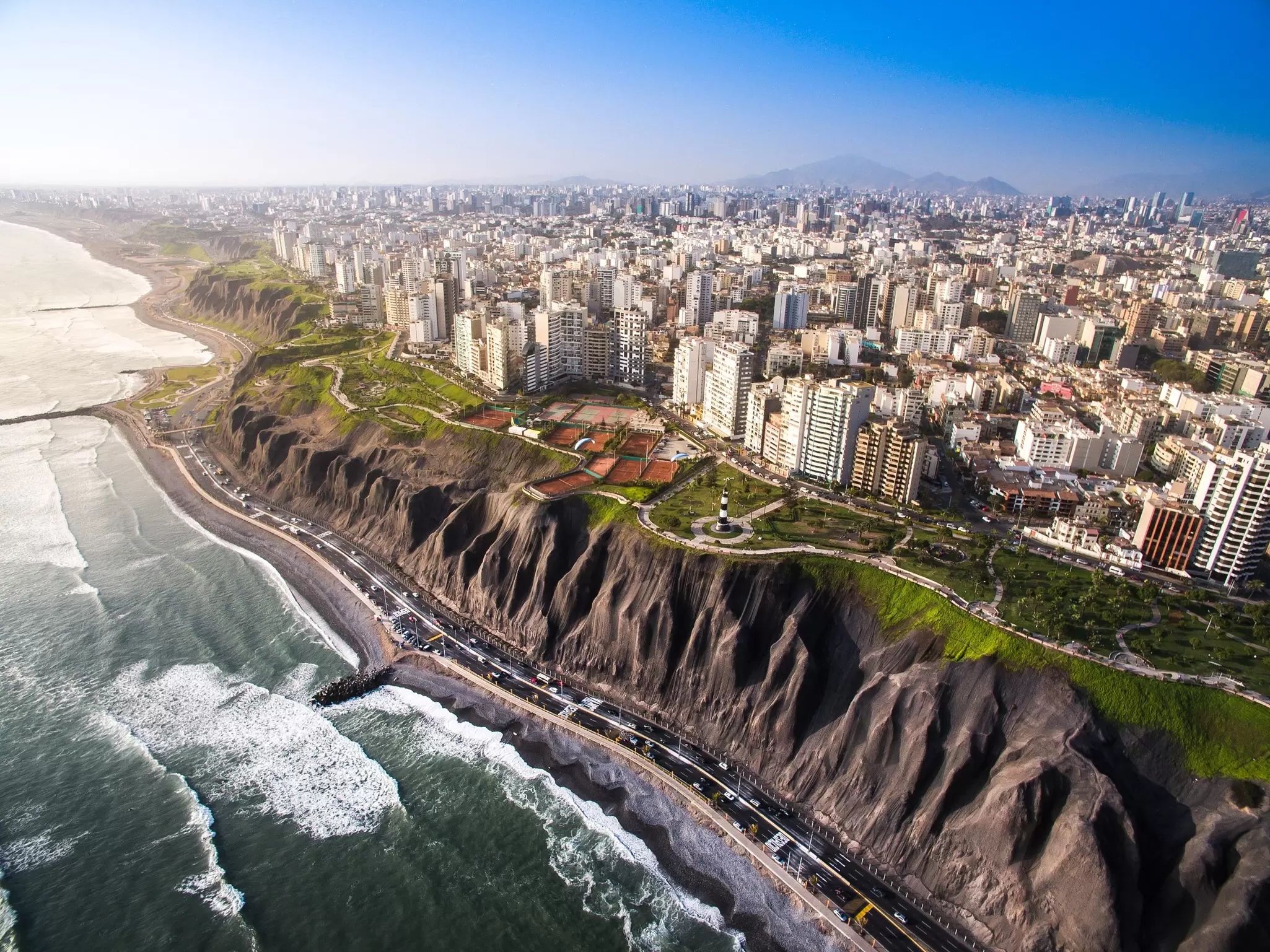 An aerial view of a city neighborhood with apartment towers that end at cliffs facing the ocean.