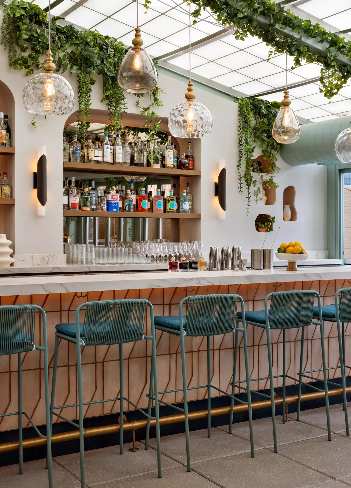Blue wire barstools are tucked under a white counter; bottles are arranged on shelves behind the bar.