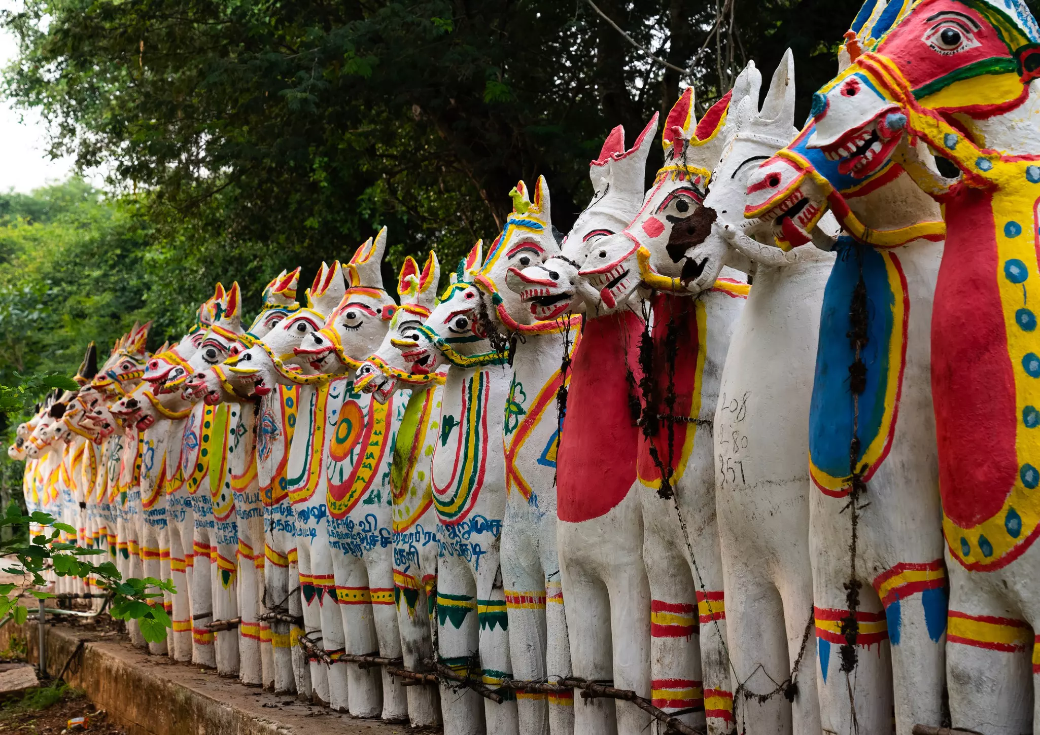 Colorfully painted terracotta horses are arranged in a tight line in front of a temple.