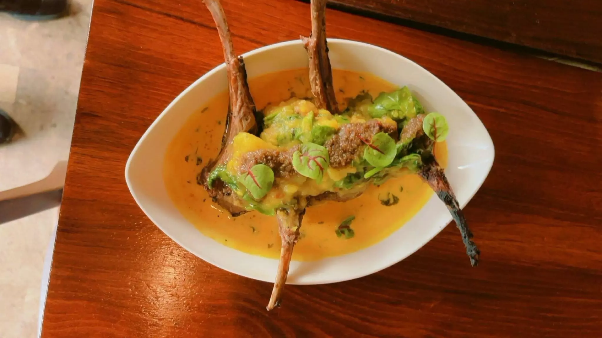 An oval dish with lamb legs in a juice topped with avocado salsa.
