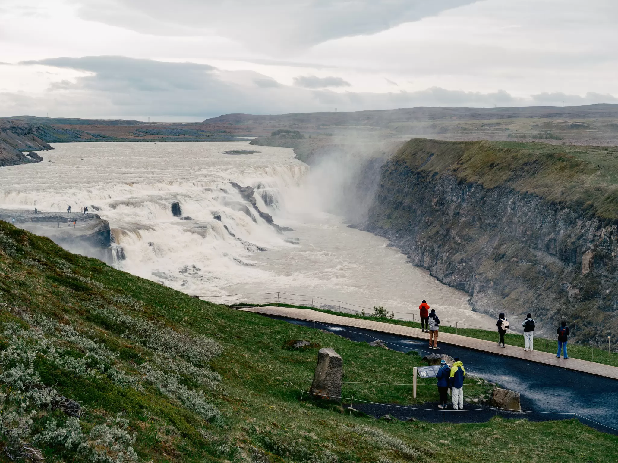 People look out from a viewing platform at Gullfoss Falls on a misty day in Iceland.