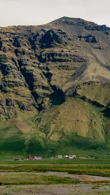 A few buildings at the base of a massive green mountain.