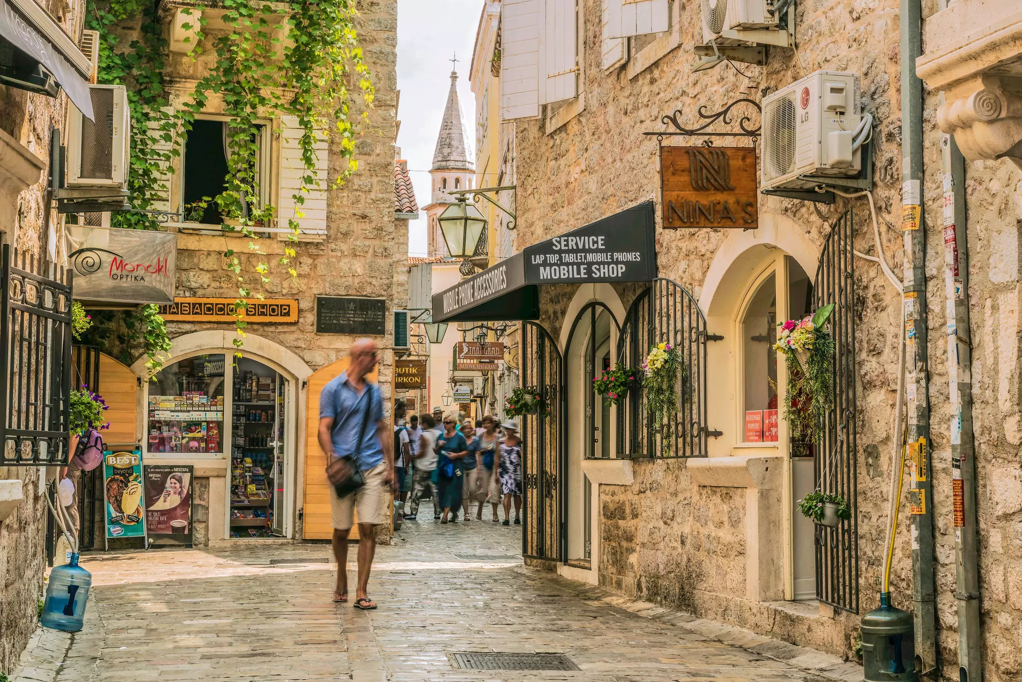 A man walking on a cobblestone street in Montenegro, looking back at a group of people behind him.