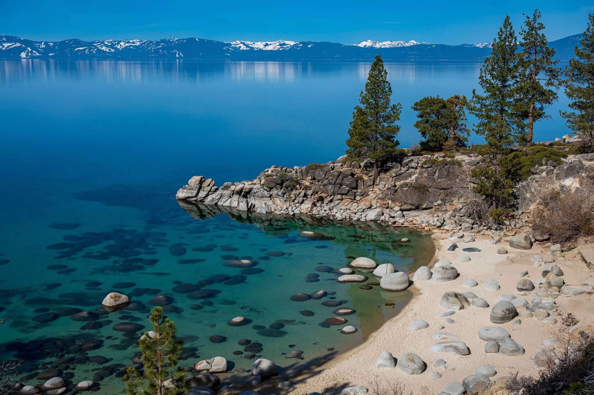 A clear blue lake with rocks in the water. Snowcapped mountains are on the far shore.