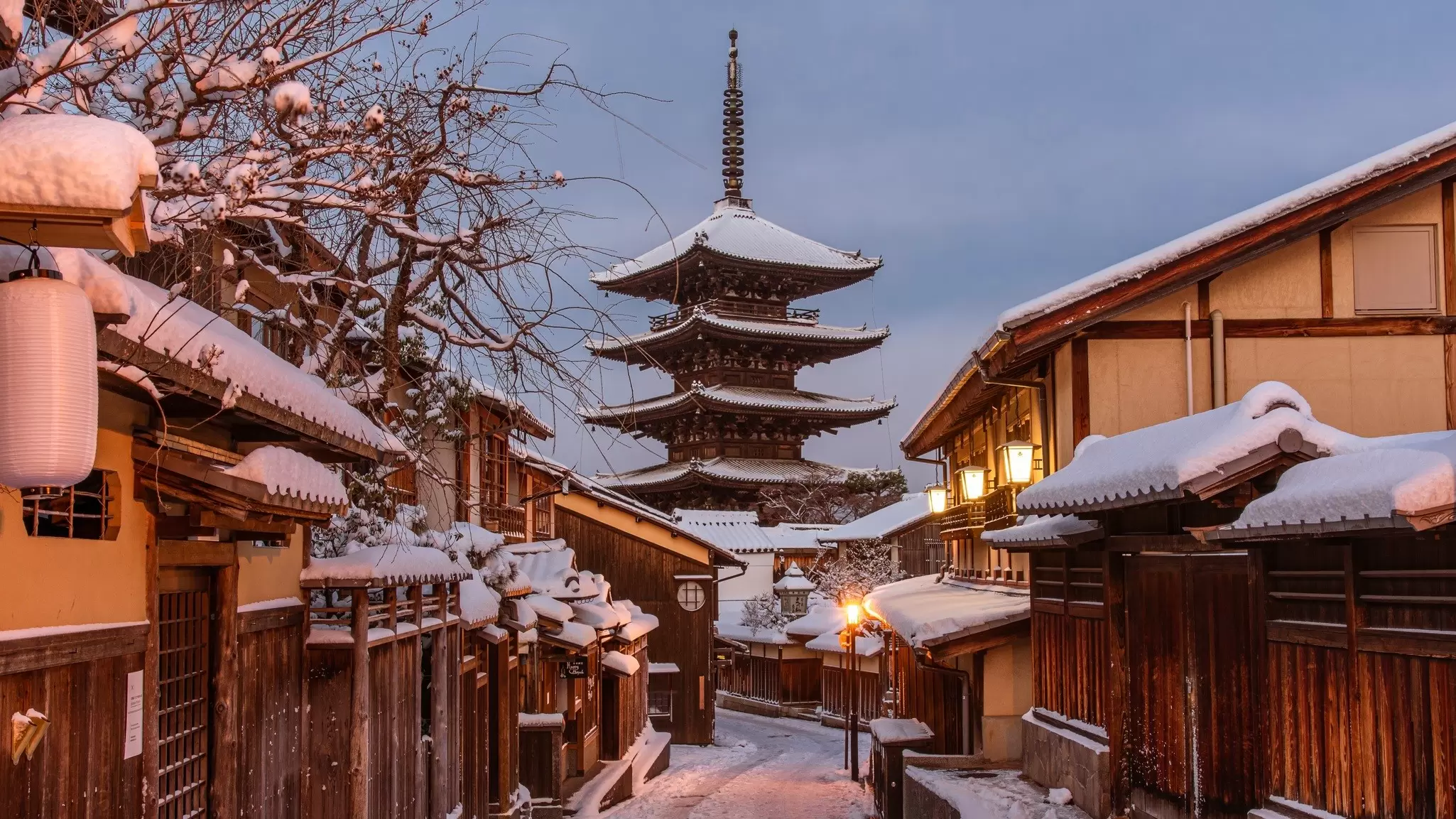 A snow-covered street with low traditional buildings leads to a four-tier pagoda with a spire.