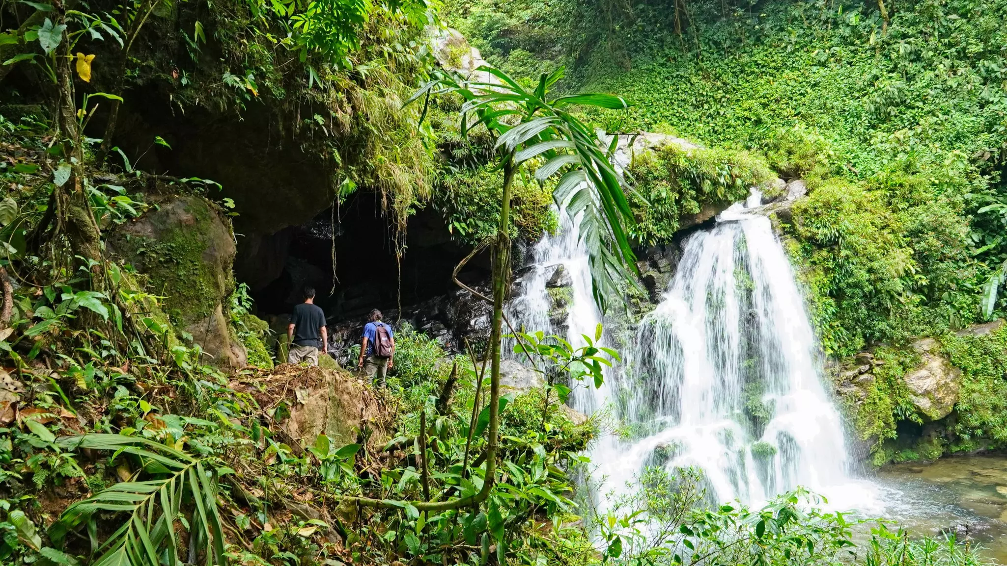 Two hikers stand near a waterfall in dense jungle in Parque Nacional Santa Fé, Panama