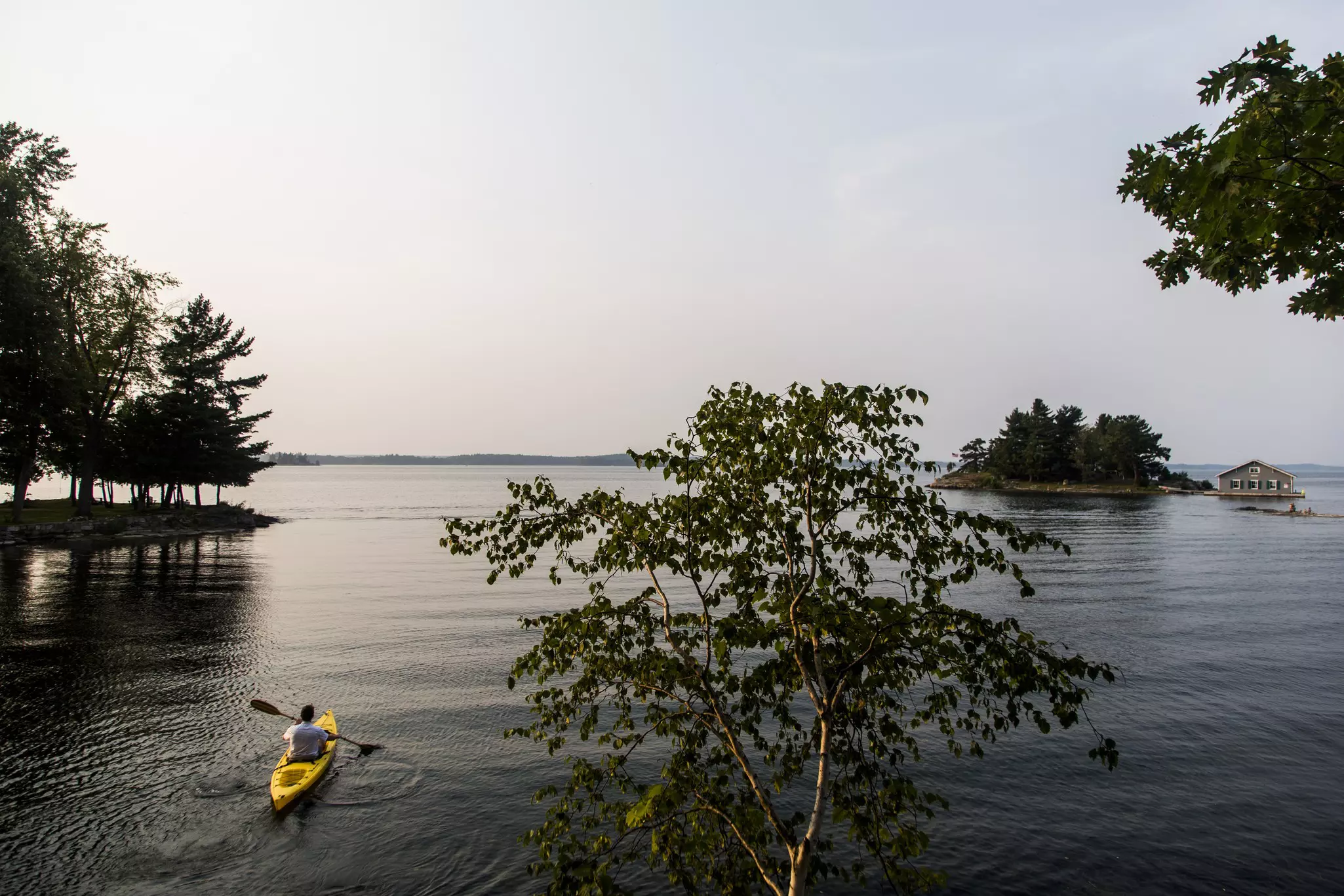 A man in a yellow kayak is seen from above as he paddles through a body of water with small tree-covered islands.