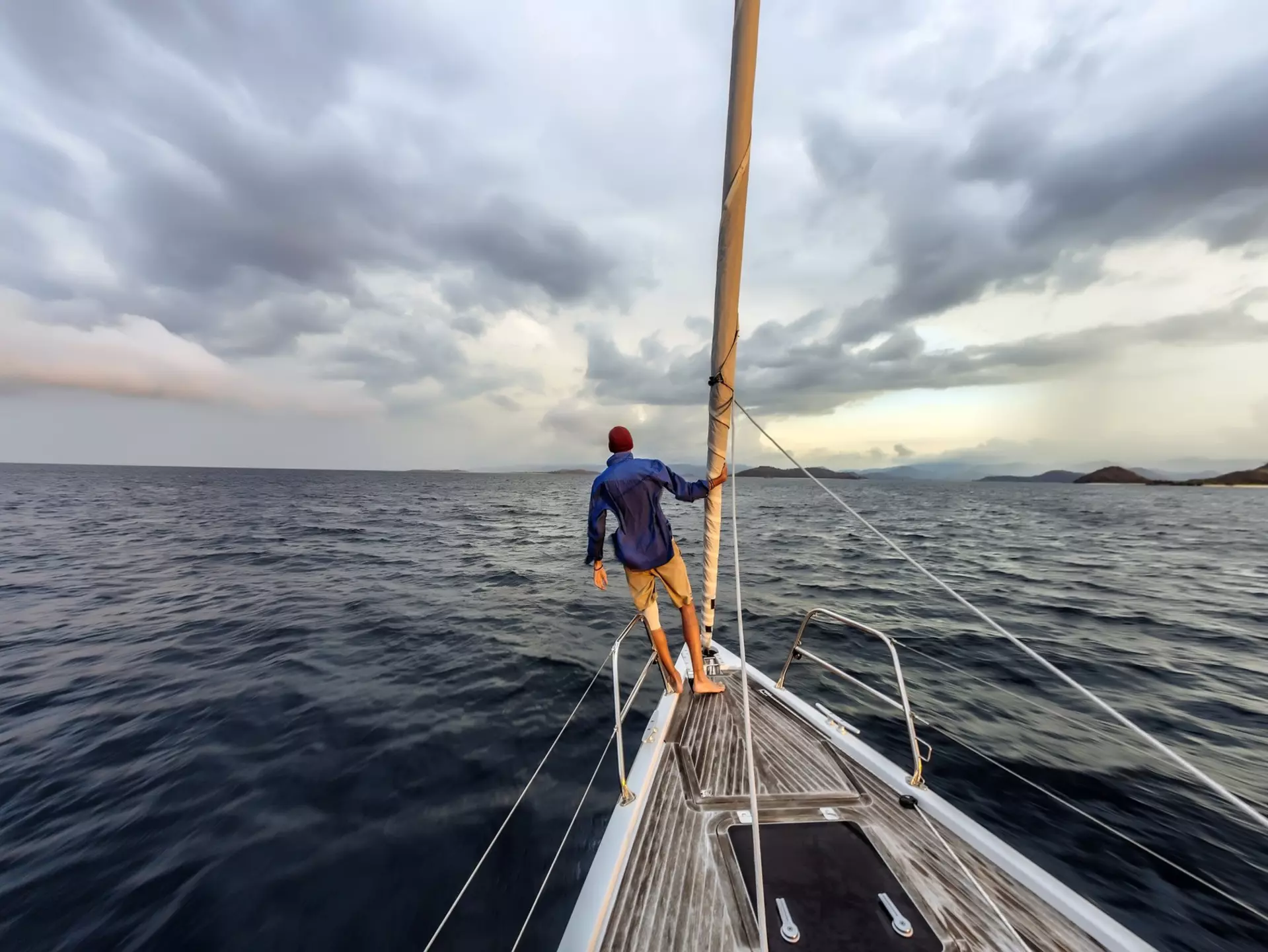 Rear view shot of single white man standing on bow of yacht looking out across Lombok, Indonesia