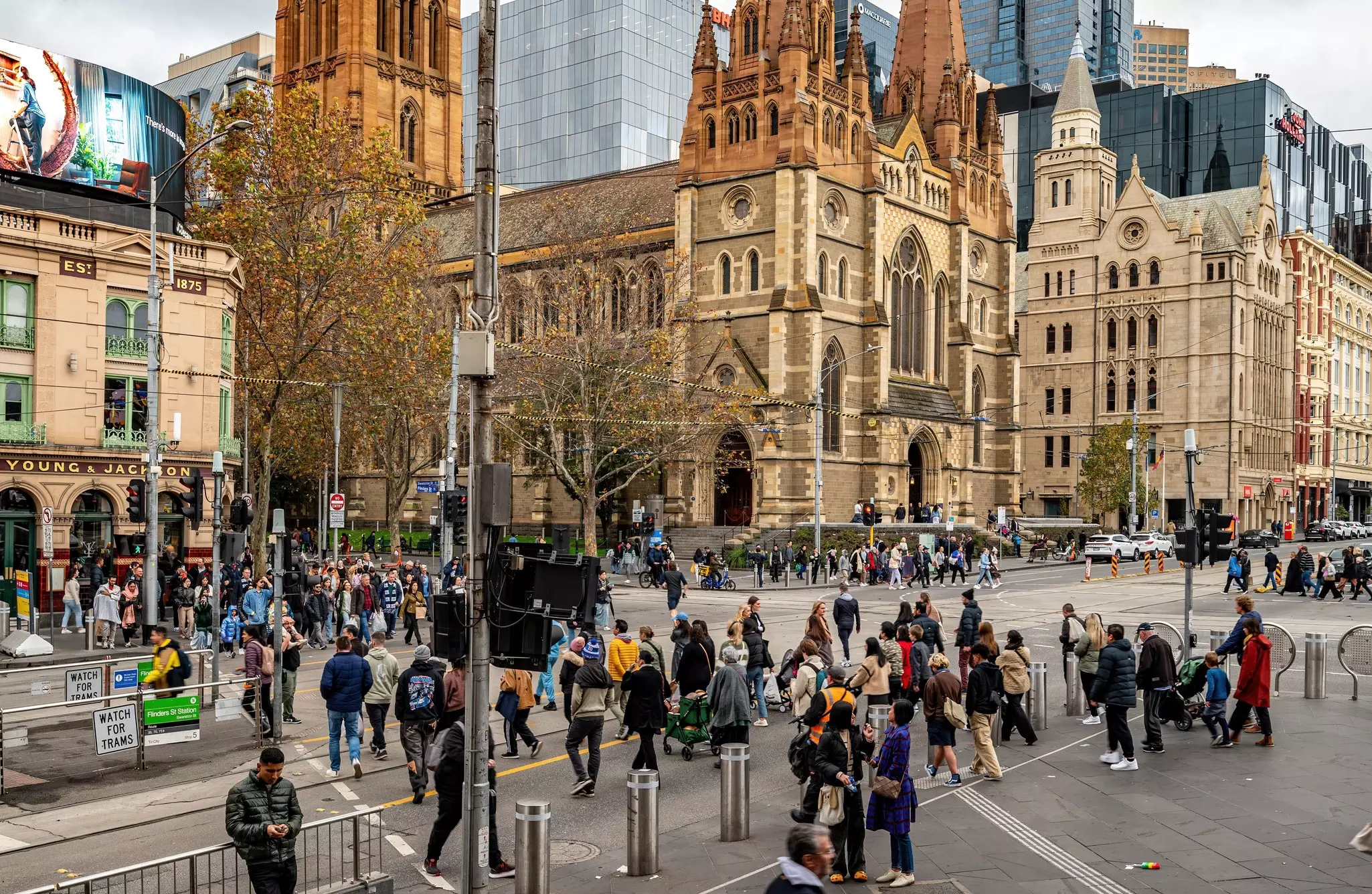 People crossing Flinders St towards Swanston St  in Melbourne's CBD with St Paul's Cathedral on one corner and Young and Jackson's pub on the other