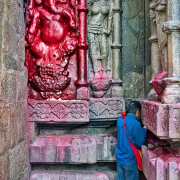 A man praying at old antique statues made in stone, on the walls inside Kamakhya Temple, where people worship mother goddess Kamakhya, in Guwahat, India.