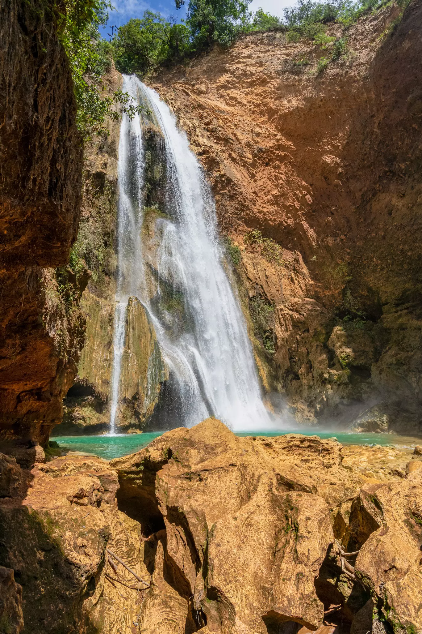 A tall waterfall cascades down a rocky cliff into a pool.
