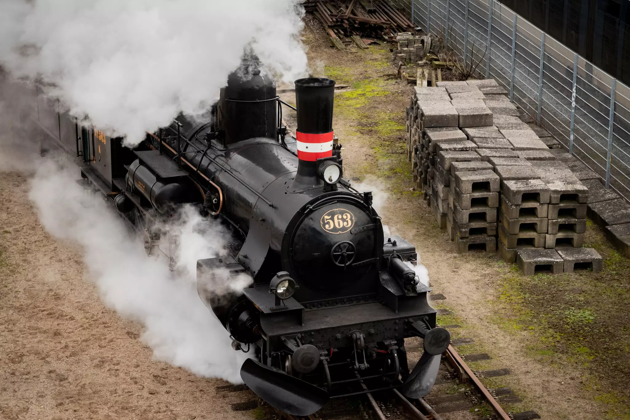 An aerial view of a restored historic locomotive billowing steam as it moves down a track.