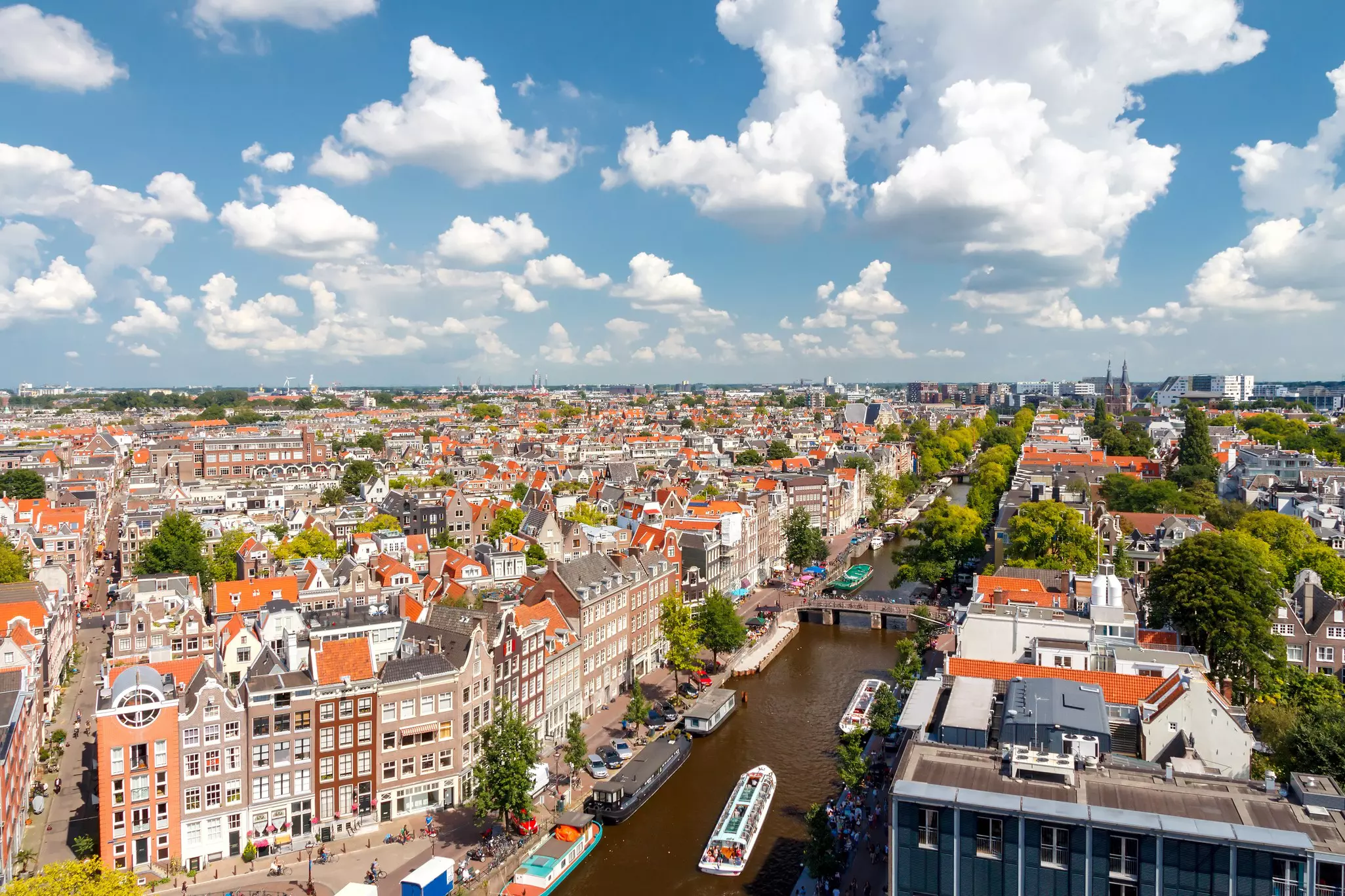 Aerial view of Amsterdam and a canal, with canal boats bordering the water and city buildings as far as the eye can see.