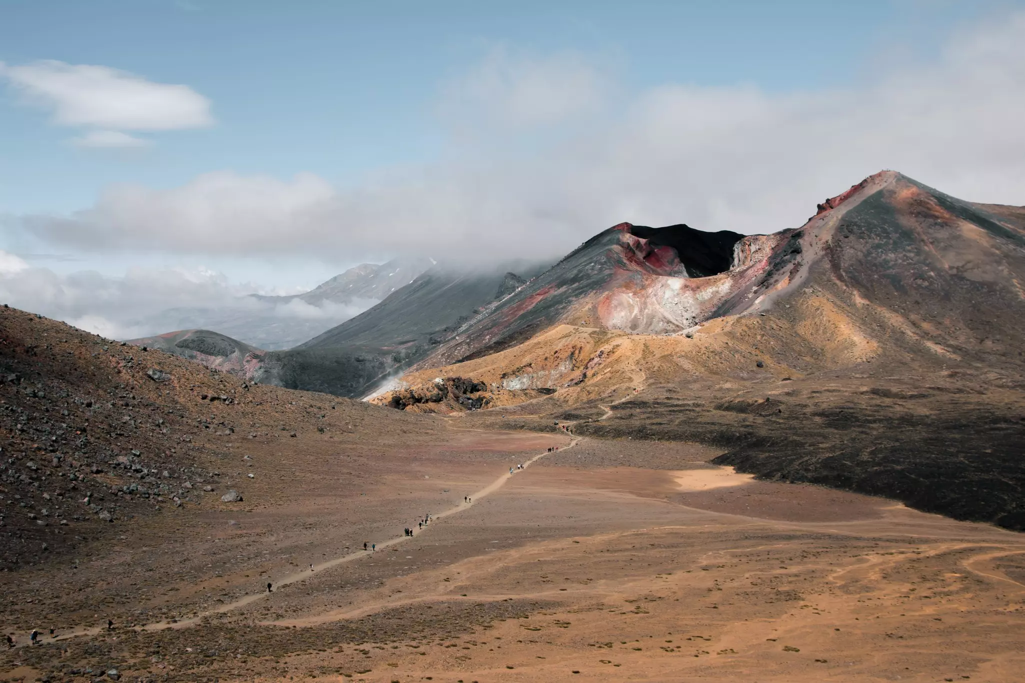 Hikers navigating a rocky pathway across a barren landscape heading towards distant mountains