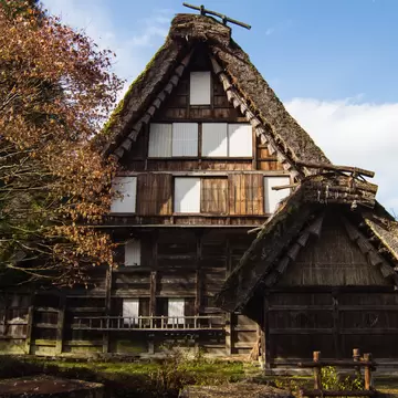 Steep thatched-roof wooden farmhouse beside autumn trees at Hida Folk Village open-air museum in Takayama