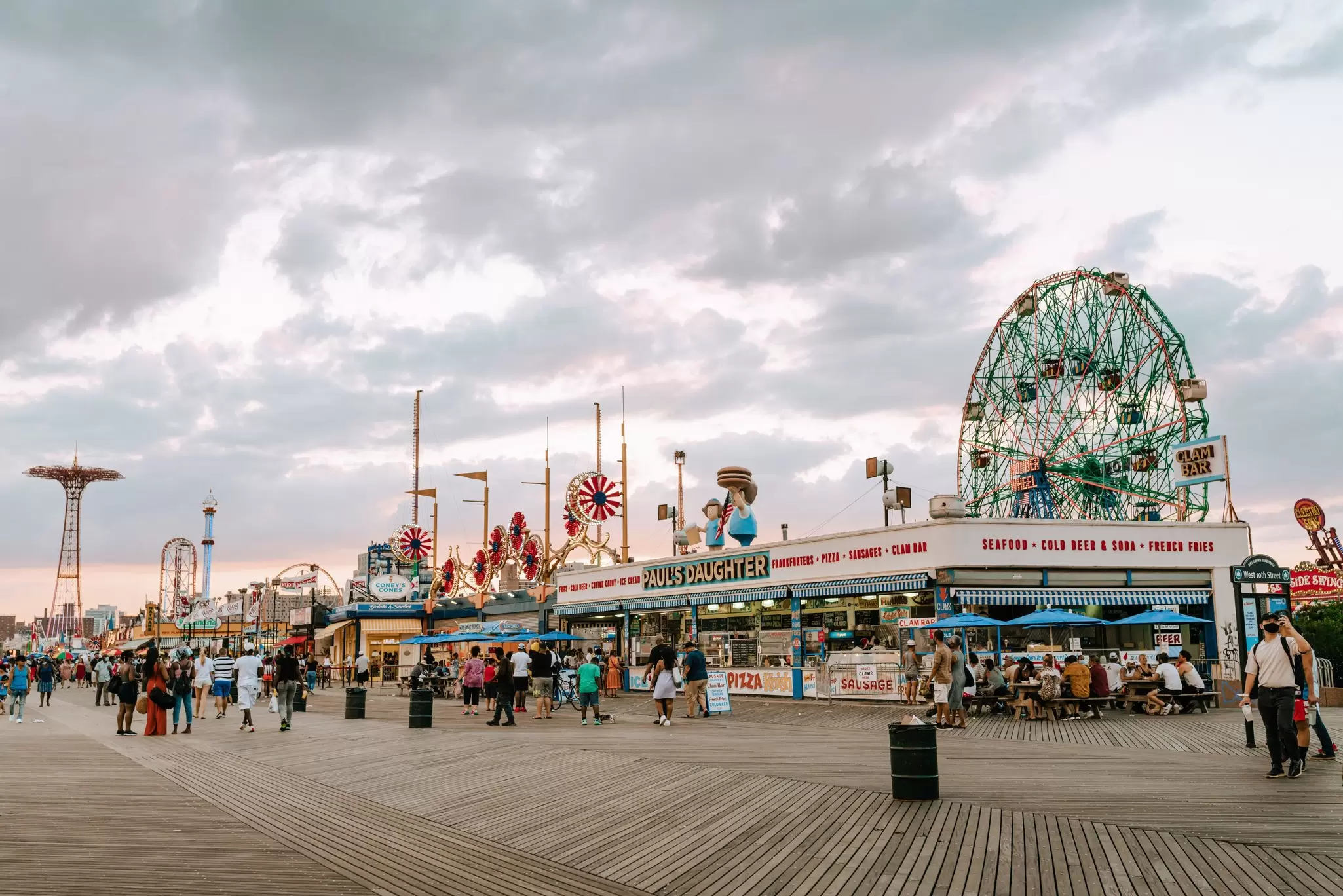Crowds of people walk down the Coney Island boardwalk of the iconic amusement park, Wonder Wheel, Brooklyn, New York.