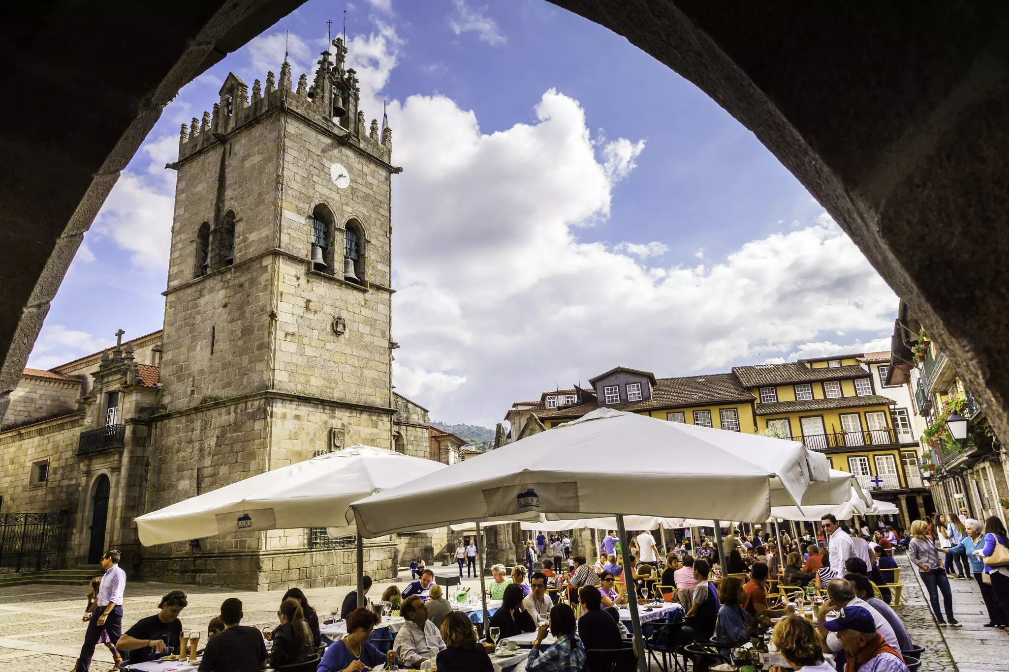 View of the Igreja de Nossa Senhora da Oliveira on the Largo da Oliveira in Guimarães, Portugal, with visitors seated in outdoor restaurants.