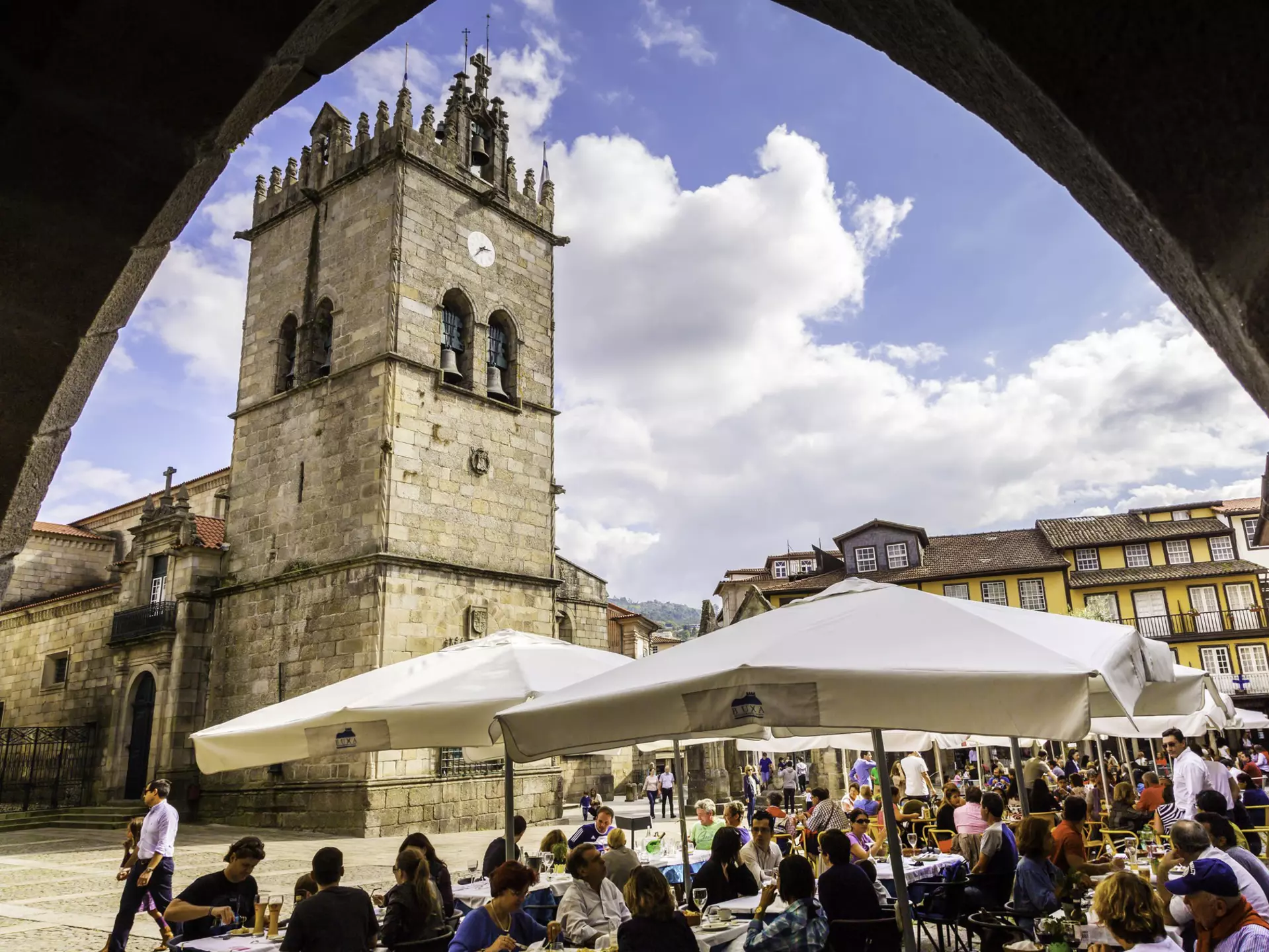 View of the Igreja de Nossa Senhora da Oliveira on the Largo da Oliveira in Guimarães, Portugal, with visitors seated in outdoor restaurants.