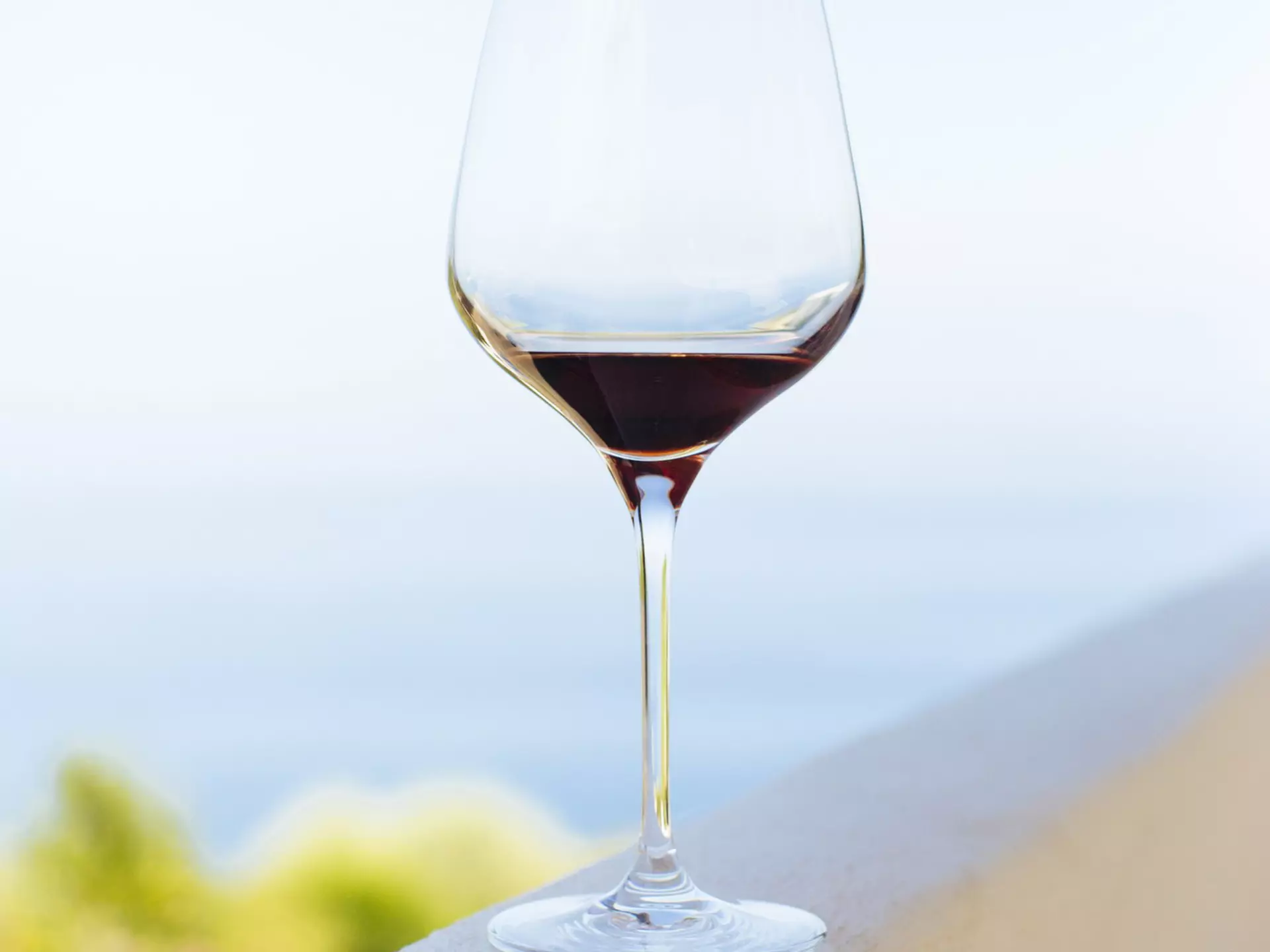 A glass of wine with a bit of wine at the bottom rests on a concrete ledge