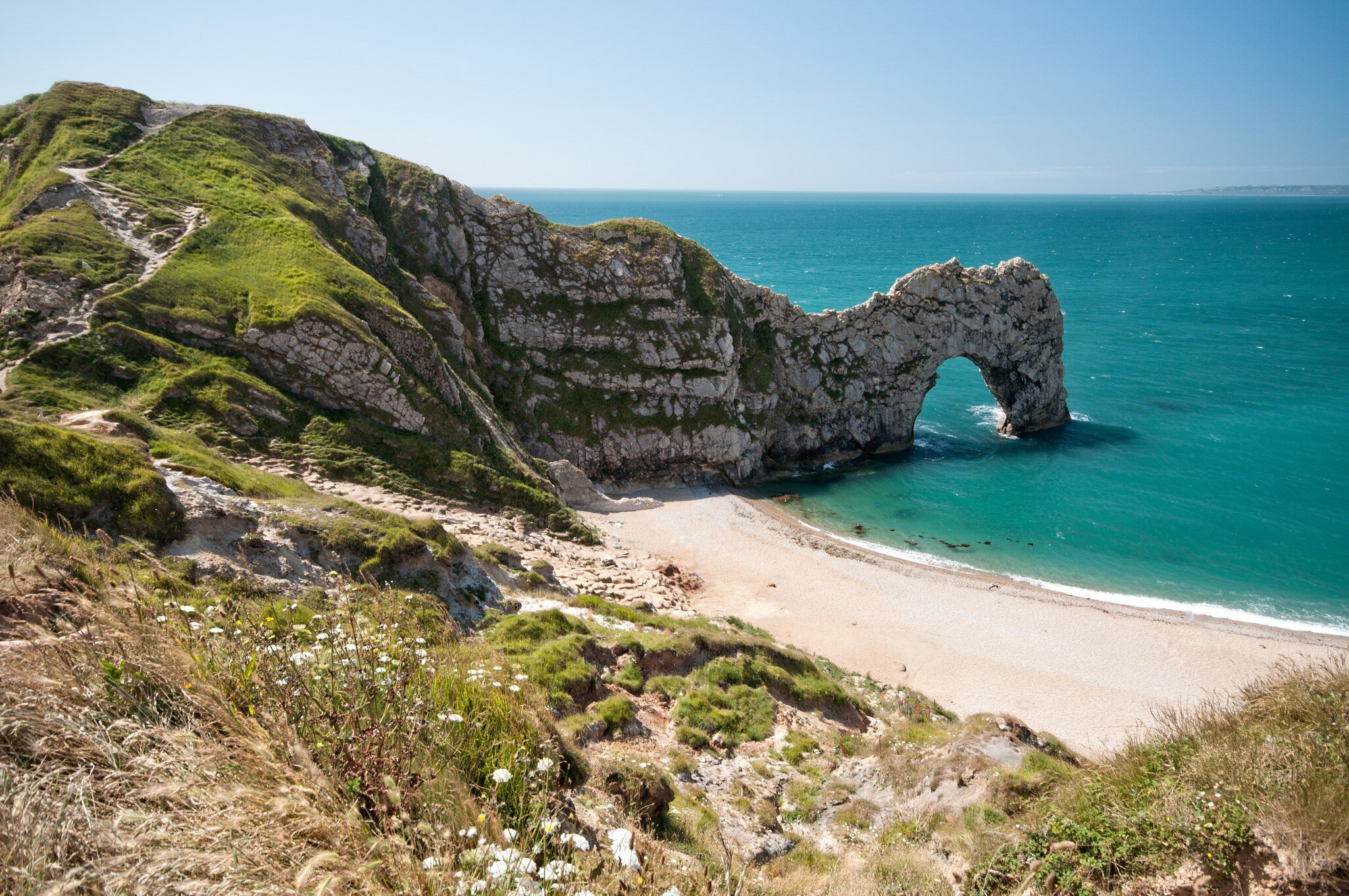 A natural limestone arch reaching into the sea beside a curving beach.