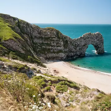 A natural limestone arch reaching into the sea beside a curving beach.