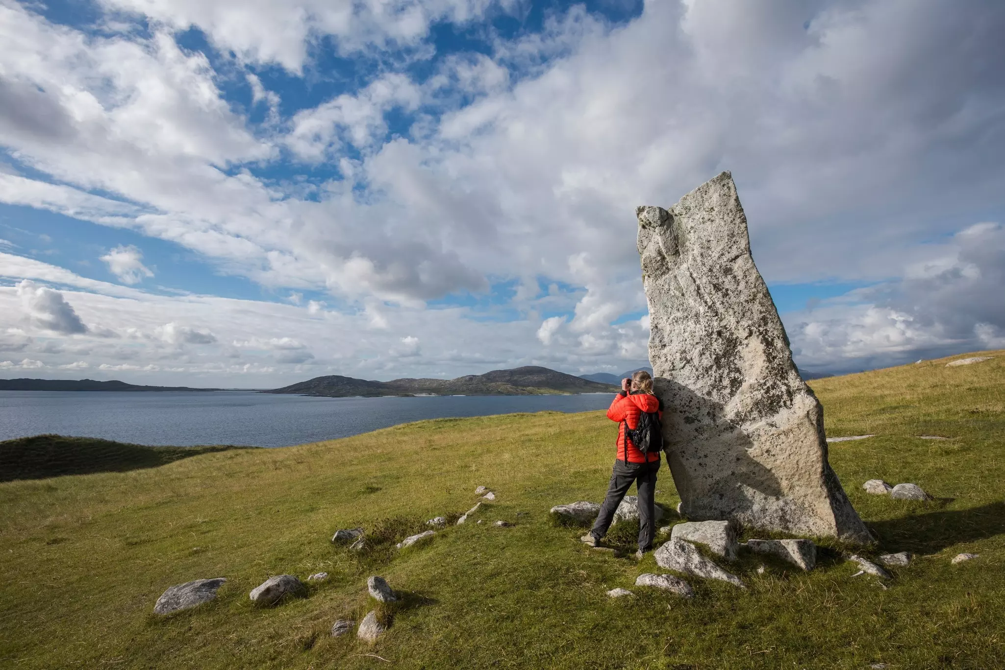 A hiker pauses by a standing stone on the Isle of Harris, Scottish Highlands.