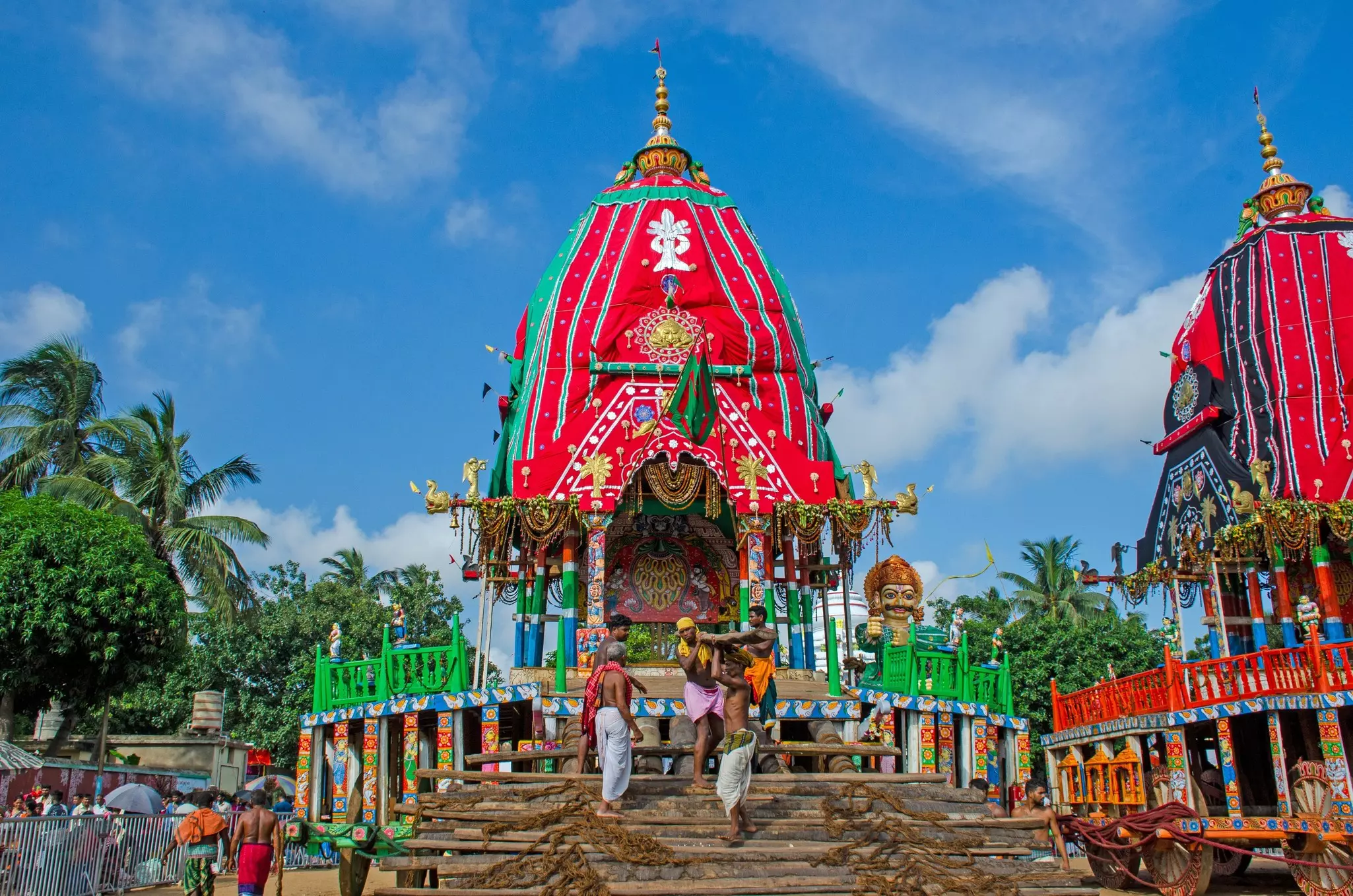People stand on steps in front of an elaborately decorated temple tower.