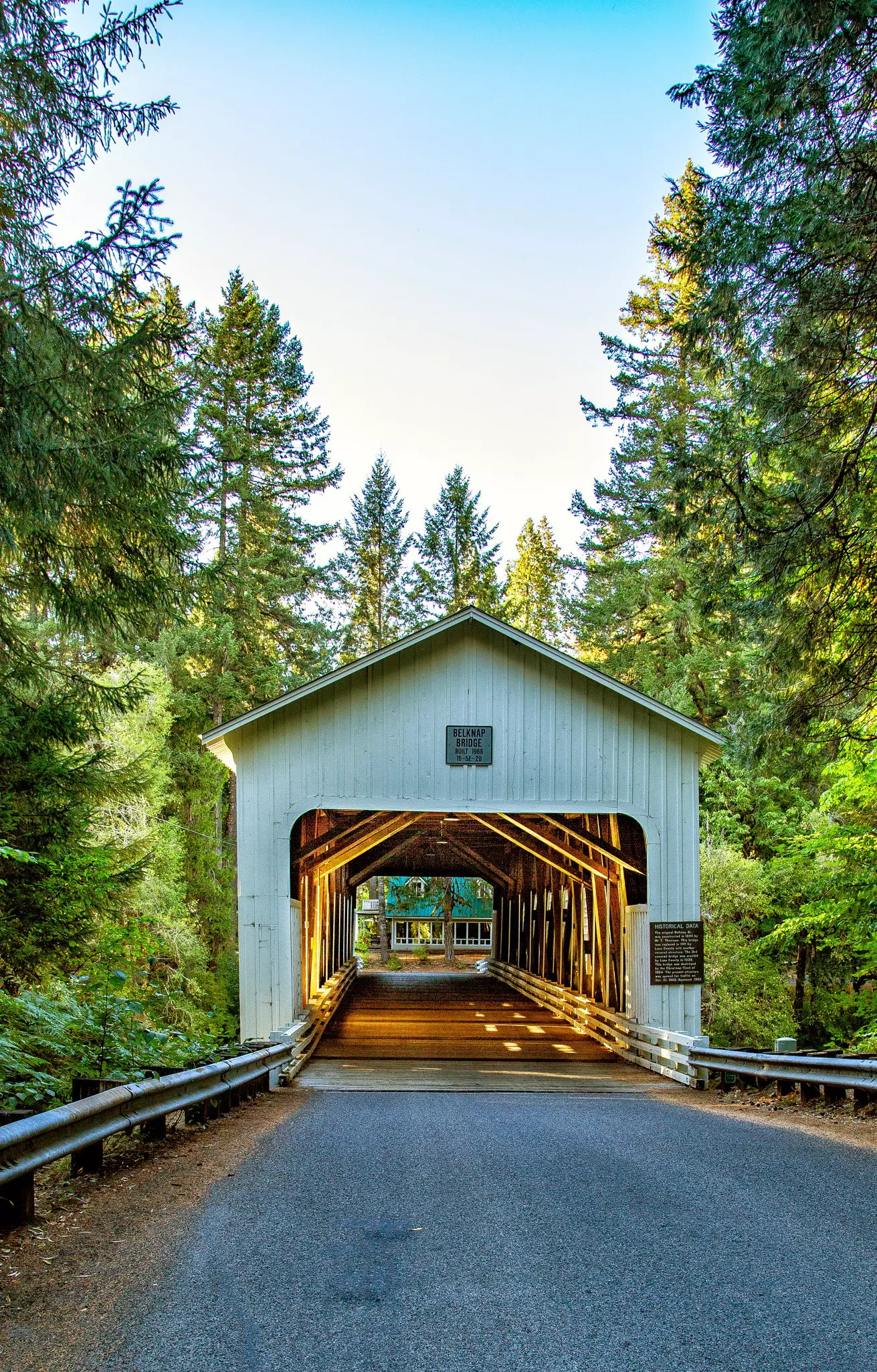 A covered bridge with forest on either side and a building at the other end on a sunny day.