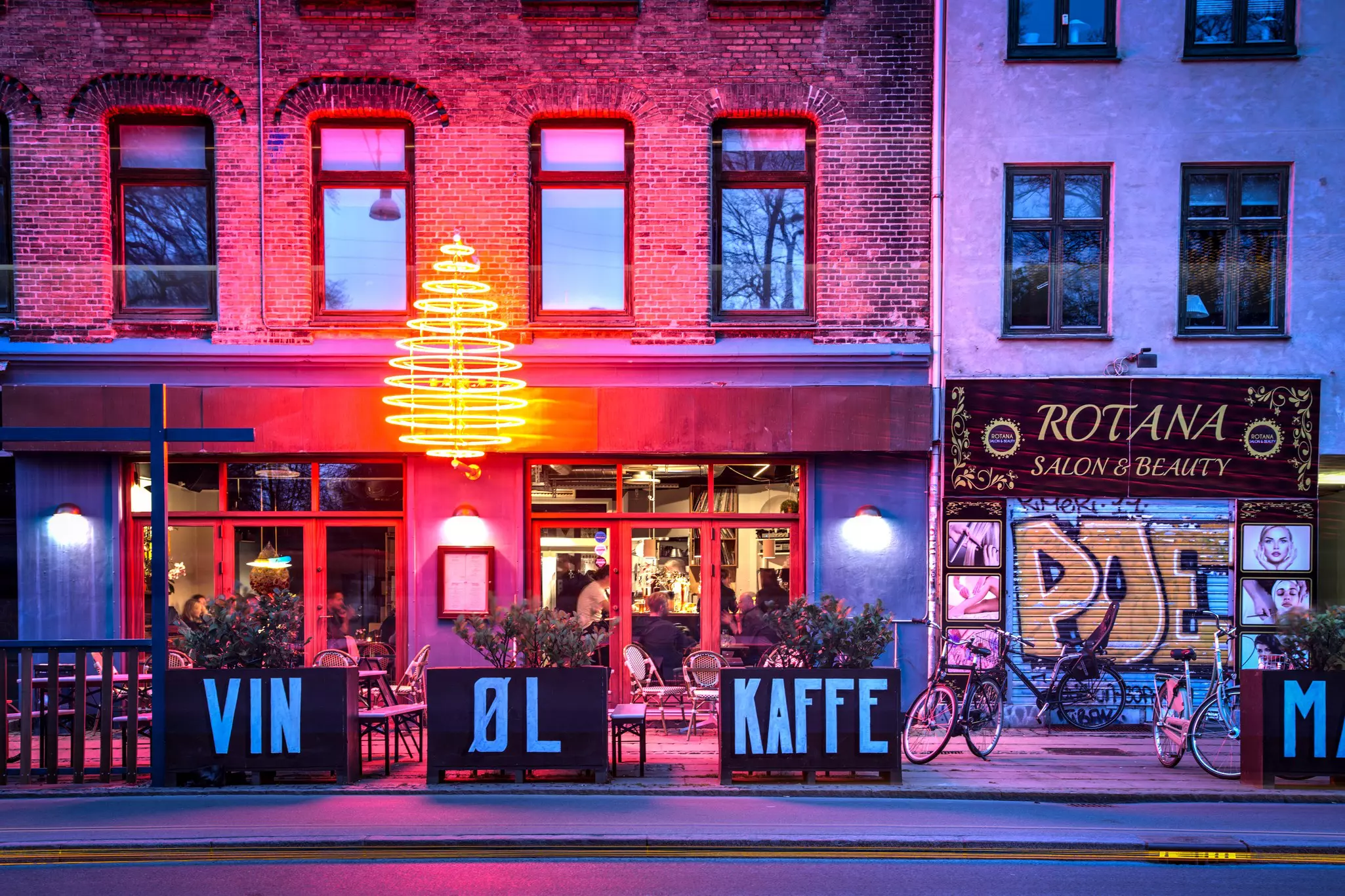 A bar lit upalongside a beauty salone on a city street at night.