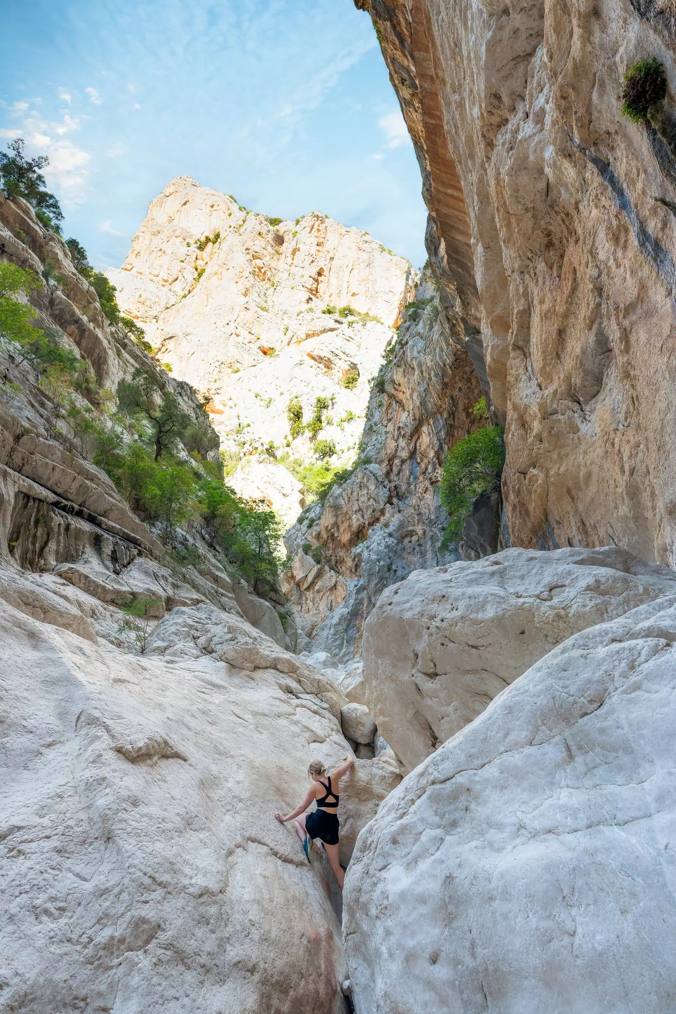 A woman climbs a massive boulder in a canyon gorge.