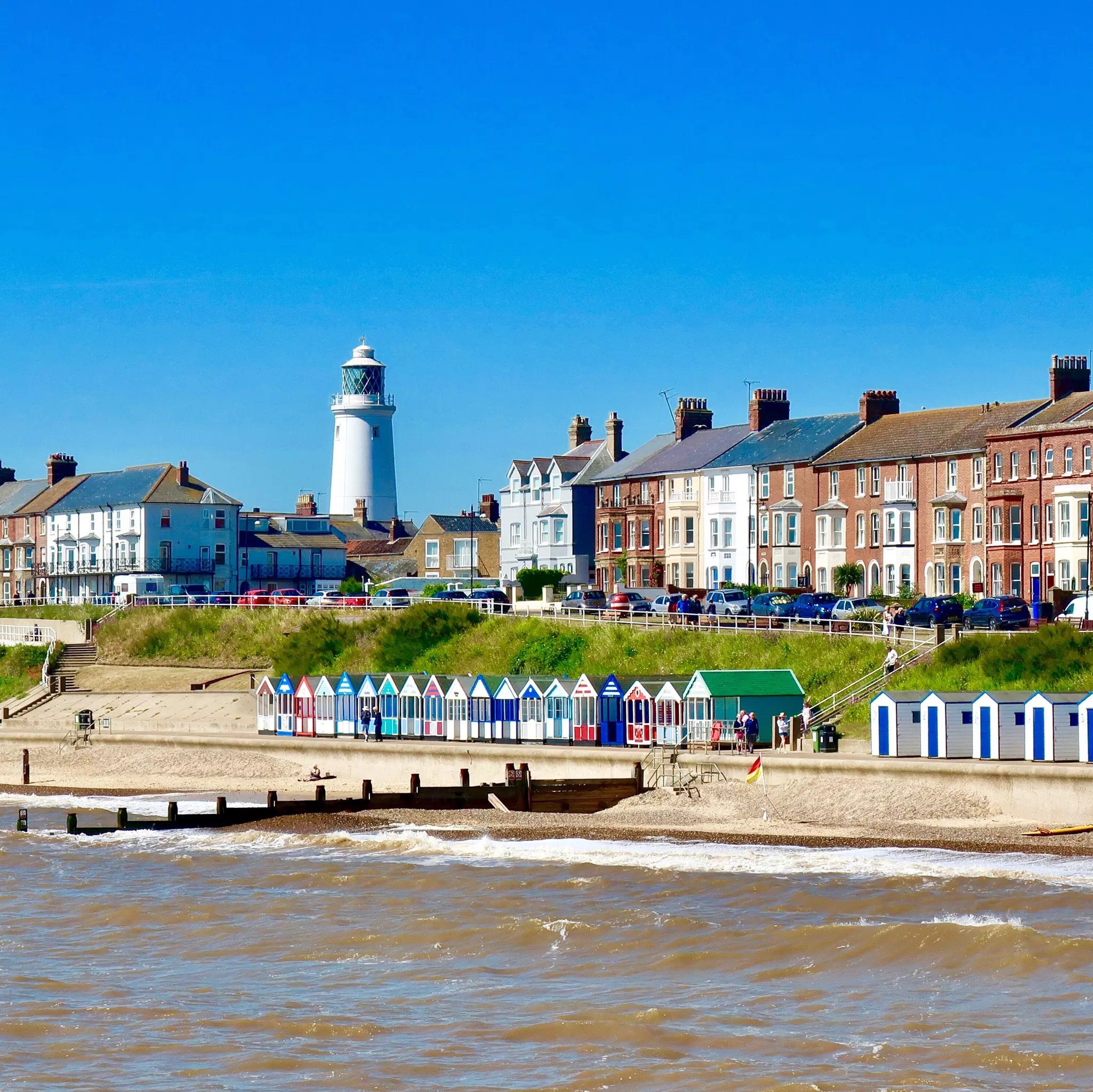 A row of colorful beach huts on a promenade below tall townhouses.