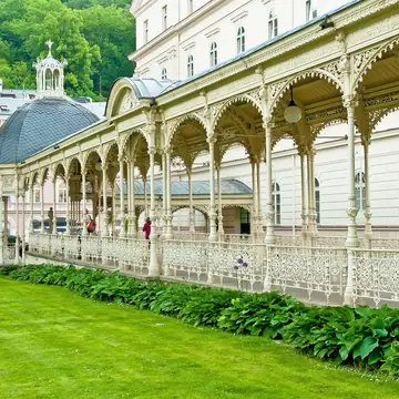 Ornate white filigree ironwork colonnade with a slate-domed pavilion beside a lawn, and an Atrium shopping centre behind