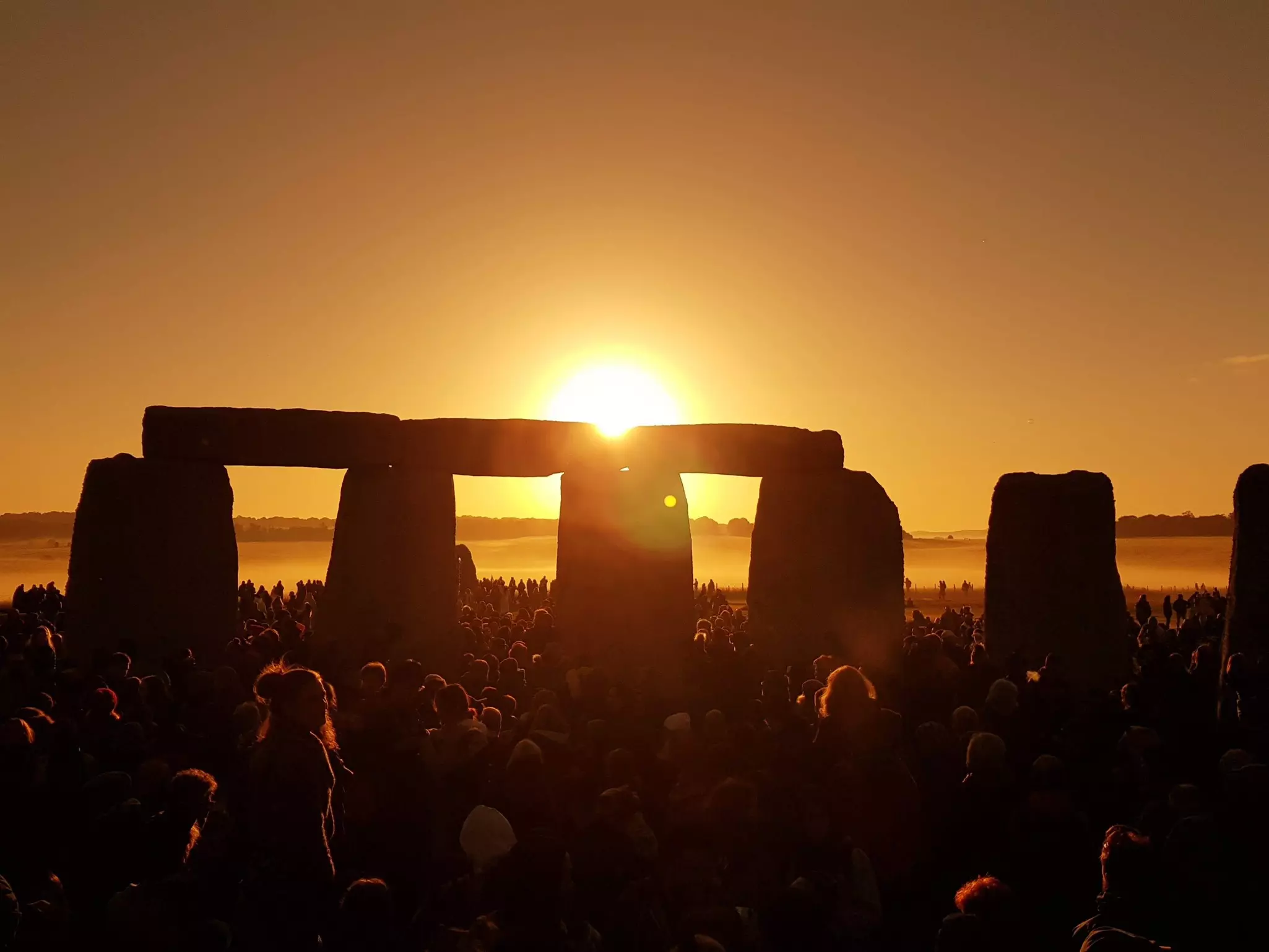 A crowd of people watch the sunrise from inside a stone circle.